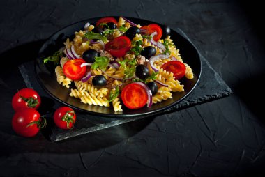 Domatesli salata, biber, ton balığı ve makarna. Siyah tabakta, siyah arka planda taze salata. Yemek yakınındaki metin için boşluk ve boş alanı kopyala.
