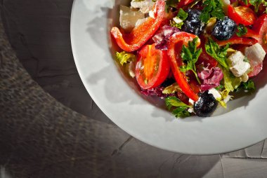 Domatesli salata, biber, zeytin, peynir ve lahana. Arka planda beyaz tabakta taze salata. Yemek yakınındaki metin için boşluk ve boş alanı kopyala.