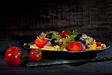 Salata, domates, biber, zeytin ve makarna. Siyah bir tabakta siyah bir arka planda taze salata..