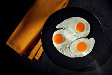 Siyah tabakta çırpılmış yumurta. Eski bir beton masada sahanda yumurta. Tabağın yanındaki sarı masa örtüsü..