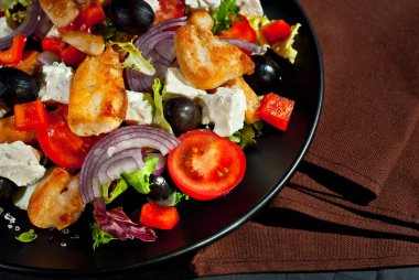 Domatesli salata, biber, zeytin ve tavuk filetosu. Siyah tabakta, siyah arka planda taze salata. Tabağın yanında kahverengi havlu var..