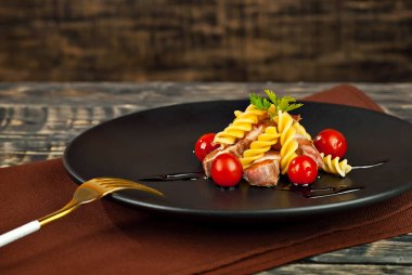 Siyah tabakta et ve domatesli makarna. Eski ahşap bir masada makarna. Sefil kahverengi arka planda bir tabak..