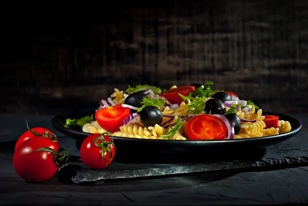 Salata, domates, biber, zeytin ve makarna. Siyah bir tabakta siyah bir arka planda taze salata..