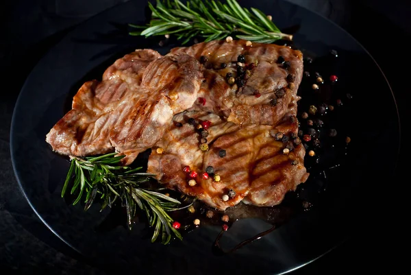 Siyah tabakta soslu biftek. Baharatlı et ve arka planda biberiye. Kontrastlı ışık sanatsal bir efekt olarak.