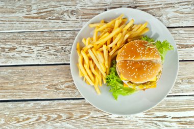 Eski püskü bir masada beyaz tabakta çizburger. Hamburger ve patates kızartması yakın mesafede. Tabağa yakın metin için boşluk ve boşluk kopyala.