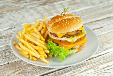Eski püskü bir masada beyaz tabakta çizburger. Hamburger ve patates kızartması yakın mesafede. Tabağa yakın metin için boşluk ve boşluk kopyala.