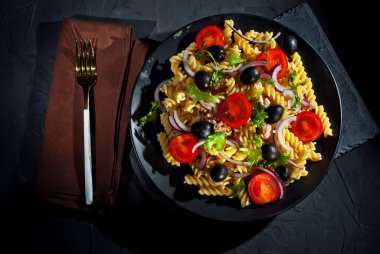 Domatesli salata, biber, ton balığı ve makarna. Siyah bir tabakta siyah bir arka planda taze salata..