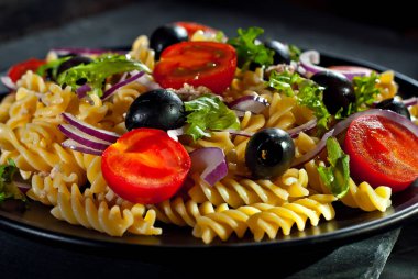 Domatesli salata, biber, ton balığı ve makarna. Siyah bir tabakta siyah bir arka planda taze salata..