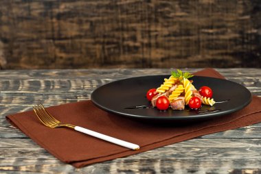 Siyah tabakta et ve domatesli makarna. Eski ahşap bir masada makarna. Kahverengi arka planda bir tabak. Yemek yakınındaki metin için boşluk ve boş alanı kopyala.