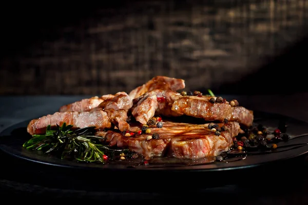 Siyah tabakta soslu biftek. Baharatlı et ve arka planda biberiye. Kontrastlı ışık sanatsal bir efekt olarak.