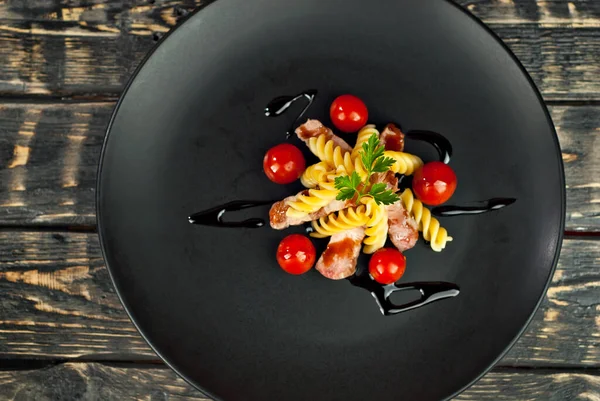 Siyah tabakta et ve domatesli makarna. Eski ahşap bir masada makarna. Sefil kahverengi arka planda bir tabak..