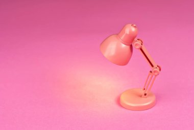 Kağıtların arka planında pembe lamba. Oyuncak masa lambası. Lambanın yanındaki metin için boşluk ve boşluk kopyala. Oda ve yaratıcı fikirler kavramı..