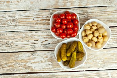 Beyaz kasede marine edilmiş domates, salatalık ve mantar. Beyaz arka planda turşulu sebzeler. Sehpada yemek. Eski ahşap bir tahtada kase.