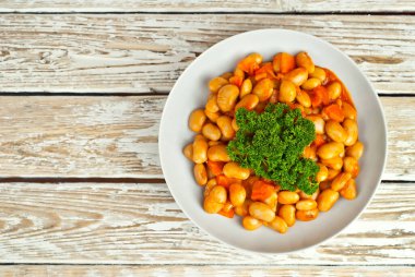 Beyaz kasede havuçlu fasulye. Beyaz arka planda fasulyeler. Sehpada yemek. Eski ahşap bir tahtanın üzerinde yuvarlan. Yemek yakınındaki metin için boşluk ve boş alanı kopyala.