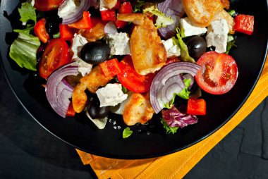 Domatesli salata, biber, zeytin ve tavuk filetosu. Siyah bir tabakta siyah bir arka planda taze salata..