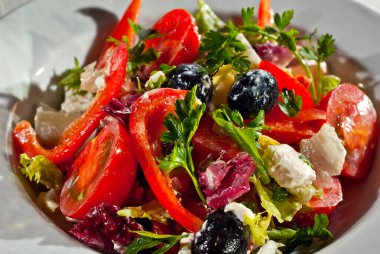 Domatesli salata, biber, zeytin, peynir ve lahana. Arka planda beyaz tabakta taze salata..