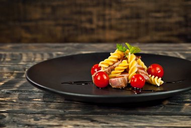 Siyah tabakta et ve domatesli makarna. Eski ahşap bir masada makarna. Sefil kahverengi arka planda bir tabak..