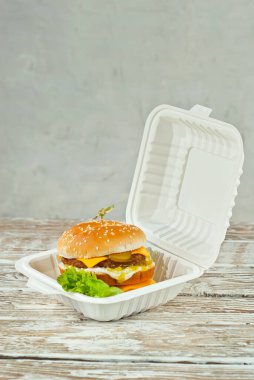 Eski püskü bir masada beyaz tabakta çizburger. Hamburger ve patates kızartması yakın mesafede. İşlenmiş mısırdan yapılmış ekolojik bir konteynırda yiyecek. Çevre dostu yemekler. Tabağa yakın metin için boşluk ve boşluk kopyala.