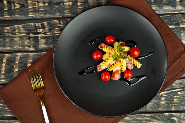 Siyah tabakta et ve domatesli makarna. Eski ahşap bir masada makarna. Sefil kahverengi arka planda bir tabak..