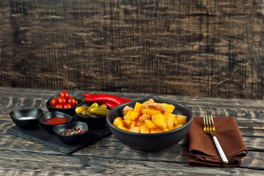 Siyah kasede etli haşlanmış patates. Siyah ahşap bir masada baharatlar ve baharatlar. Eski püskü bir arka planda ketçap, tuz ve biber..