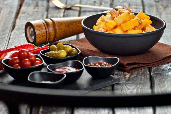 Siyah kasede etli haşlanmış patates. Siyah ahşap bir masada baharatlar ve baharatlar. Eski püskü bir arka planda ketçap, tuz ve biber..