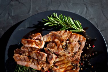 Siyah tabakta soslu biftek. Baharatlı et ve arka planda biberiye. Kontrastlı ışık sanatsal bir efekt olarak.