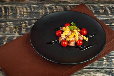 Siyah tabakta et ve domatesli makarna. Eski ahşap bir masada makarna. Sefil kahverengi arka planda bir tabak..