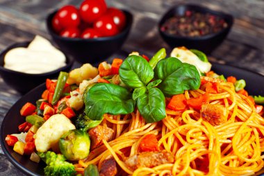 Siyah tabakta havuçlu, sebzeli ve etli erişte. Siyah Erivan masasında yemek. Makarnada fesleğen yaprağı. Sebze karışımlı makarna. Arka planda domates ve baharat turşusu.