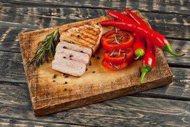 Kesme tahtasında dilimlenmiş domatesli biftek. Koyu ahşap arka planda et. Yemek, sos, tuz, biber ve baharatlar eski püskü bir masada..