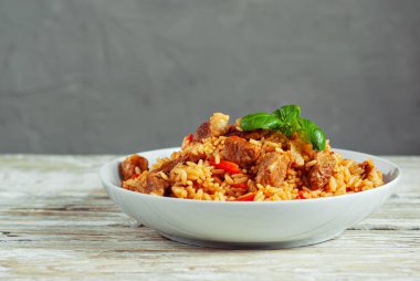 Pilaf beyaz bir plaka ve hafif bir arka plan. Tahtada fesleğenli pirinç. Sefil ahşap masada yemek..