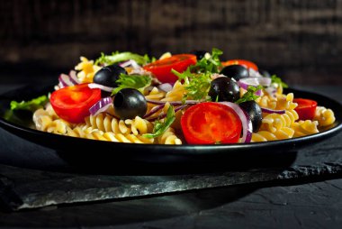 Domatesli salata, biber, ton balığı ve makarna. Siyah bir tabakta siyah bir arka planda taze salata..
