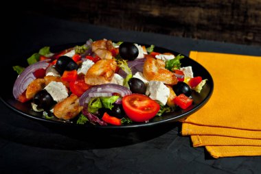 Domatesli salata, biber, zeytin ve tavuk filetosu. Siyah tabakta, siyah arka planda taze salata. Tabağın yanında sarı havlu var..