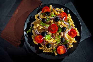 Domatesli salata, biber, ton balığı ve makarna. Siyah bir tabakta siyah bir arka planda taze salata..
