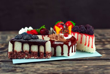 Siyah arka planda farklı pastalar. Çikolatalı ve meyveli kek parçaları. Kahverengi ahşap masadaki şekerler.