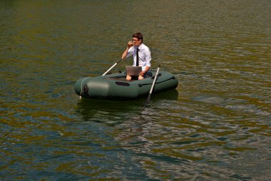 Şişme teknede beyaz gömlekli bir adam. Göl kenarında dizüstü bilgisayarı olan bir iş adamı. Uzaktan çalışma, boş zaman ve serbest çalışma kavramı..