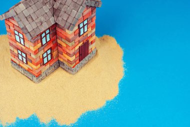 Kumda bir ev maketi. Deniz ve mavi gökyüzünün arka planında bir sahil evi. Ev ve ipotek konsepti. Evin yakınındaki cennet adası..