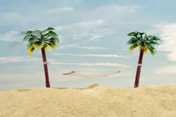 人工のヤシの木にミニチュアハンモック 砂の中にヤシの木とビーチのレイアウト 背景に青い空 休息旅行の概念 — ストック写真
