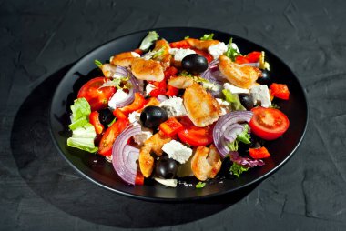 Domatesli salata, biber, zeytin ve tavuk filetosu. Siyah bir tabakta siyah bir arka planda taze salata..
