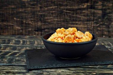 Siyah kasede et ve havuçlu pilav. Siyah arka planda Pilaf. Sehpada yemek. Eski ahşap bir tahtanın üzerinde yuvarlan. Yemek yakınındaki metin için boşluk ve boş alanı kopyala.