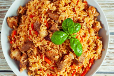 Pilaf beyaz bir plaka ve hafif bir arka plan. Tahtada fesleğenli pirinç. Sefil ahşap masada yemek. Üst görünüm.