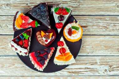 Beyaz arka planda farklı pastalar. Çikolatalı ve meyveli kek parçaları. Pejmürde bir masa üzerindeki şekerler.