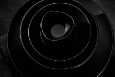 Siyah masa takımı koyu bir arka planda. Tabaklar ve kaseler farklı şekil ve boyutlarda yığılmış. Sanatsal bir efekt olarak dramatik ışık karşıtlığı.