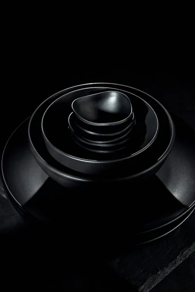 深色背景下的黑色餐具 不同形状和尺寸的盘子和碗堆在一起 对比戏剧性的光作为一种艺术效果 — 图库照片
