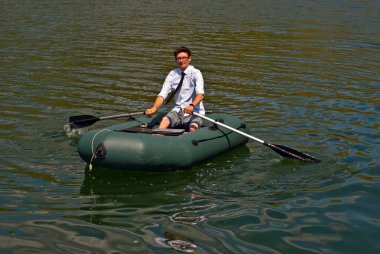 Şişme teknede beyaz gömlekli bir adam. Göl kenarında dizüstü bilgisayarı olan bir iş adamı. Uzaktan çalışma, boş zaman ve serbest çalışma kavramı..