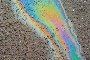 Islak asfaltta yağ lekeleri var. Su birikintileri çok renkli petrol akıntılarıyla kirlenmiş. Çevre kirliliği, petrol sızıntıları ve çevre sorunları kavramı.