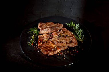 Siyah tabakta soslu biftek. Baharatlı et ve arka planda biberiye. Kontrastlı ışık sanatsal bir efekt olarak.