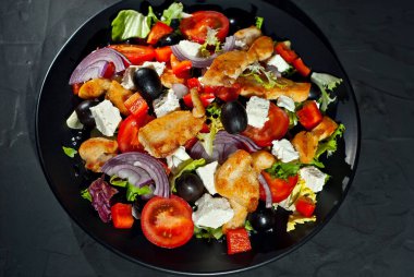 Domatesli salata, biber, zeytin ve tavuk filetosu. Siyah bir tabakta siyah bir arka planda taze salata..