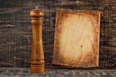 Siyah, pejmürde bir masada kesme tahtası ve tuzluk. Karanlık bir arka planda biber parçala. Yemek pişirme araçlarının yakınındaki figüranlar için boşluk ve boşluk kopyala. Tuz makinesinde keskinlik.