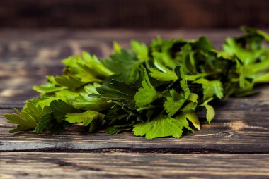 Siyah ahşap bir masada maydanoz. Maydanoz sürüsü koyu bir arkaplanda. Eski püskü bir kalbe yeşiller.