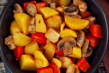 Siyah kasede etli haşlanmış patates. Mantarlı ve havuçlu patates. Haşlanmış mantar ve patatesli tavuk. Siyah ahşap bir masada yemek. 